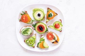 Set of vegetarian sandwiches on white plate on white textured background.