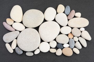 Top view of arranged pebble stones on black slate background