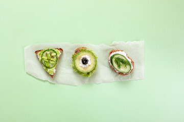 Three vegetarian sandwiches on parchment paper piece in center of green background.