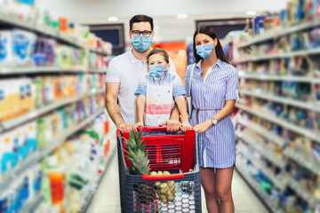 Happy family wearing face protective medical masks for protection from virus disease with shopping cart buying food at supermarket. New normal.