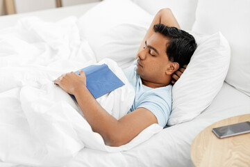 people, bedtime and rest concept - indian man with book sleeping in bed at home