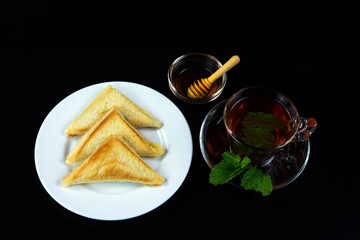 Homemade toasted bread on white plate, black tea with honey and mint leaves.