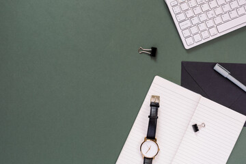 Top view of modern office desk with copy space. Empty weekly planner, keyboard, watch, stationery on pastel green background.