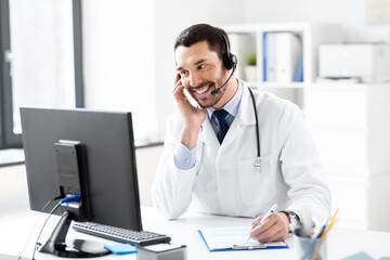 healthcare, medicine and technology concept - happy smiling male doctor with headset, computer and clipboard working at hospital