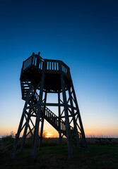 A man enjoying the evening view  from an wildlife observation tower in a nature area.