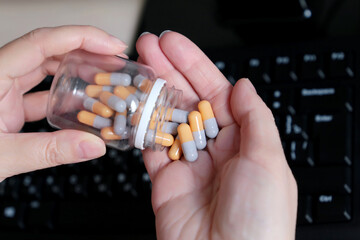 Bottle of pills in female hands on PC keyboard background. Woman with medication in capsules, concept of overwork and stress in the office, taking vitamins