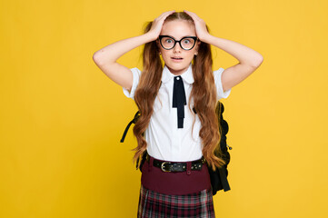 Naklejka premium Surprised schoolgirl wearing uniform and glasses with backpack on vivid bright yellow background, caucasian elementary pupil, education school concept