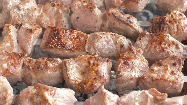 Closeup 1080p shot of the pork meat on skewers roasting on a charcoal barbecue grill, taken with a macro lens