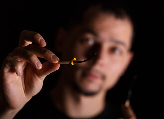 Fototapeta premium Dark portrait of a man with burning match and blurred face