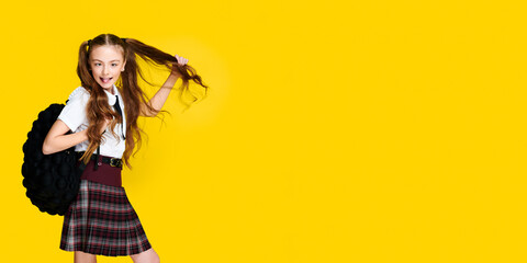 Elementary schoolgirl with backpack on vibrant yellow background, pupil in uniform, banner format, education concept