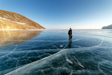 Lonely girl standing on frozen Baikal lake covered with clear ice