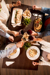 Naklejka na ściany i meble Four hands with red wine toasting over served table with food