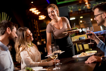 Waiter woman serving group of friends with food in the restaurant