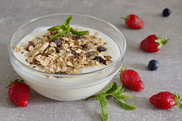 Transparent bowl with oat flakes, yogurt, strawberries, blueberries and mint leaves on kitchen desk