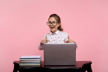 A young girl sits at a laptop in a white shirt and black-rimmed glasses