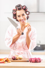 Beautiful girl stands smiling at the camera holding onion in one hand and knife in the other one
