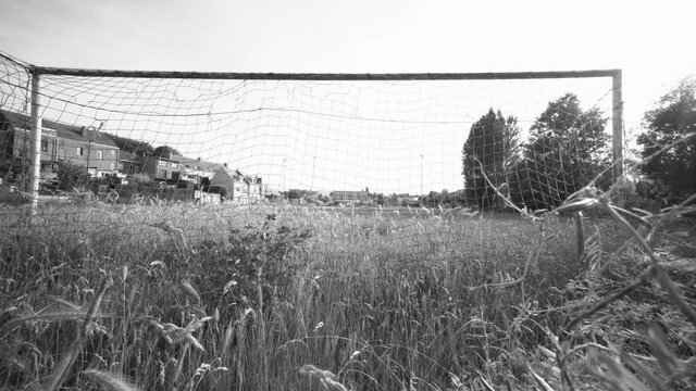High uncut wild grass on soccer field. Inactivity on the pitch because of corona. Wide angle behind the goal. Black and white.