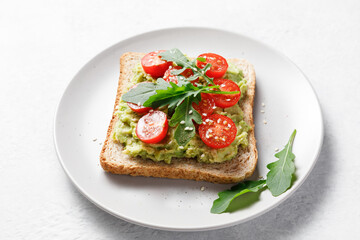Fototapeta na wymiar Avocado rye bread toast with cherry tomatoes and arugula on bright background.