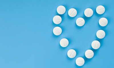 White pills laid out in the form of a heart on a blue background close-up.