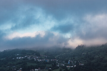 Landscape of cloudy mountains and a small town surrounded by forests and meadows