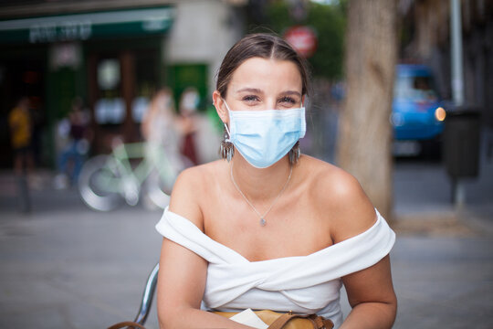 Chica joven con mascarilla en una terraza en la calle