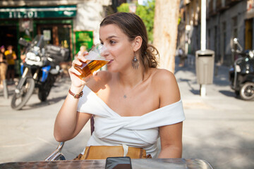 Chica rubia bebiendo cerveza en una terraza de un bar