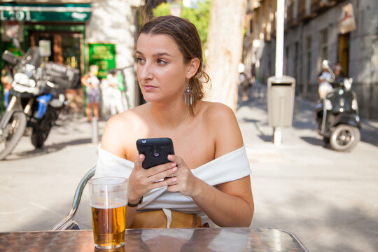 Chica joven usando el móvil en una terraza de un bar