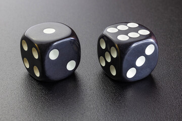 Two black dice close-up on a dark illuminated surface.