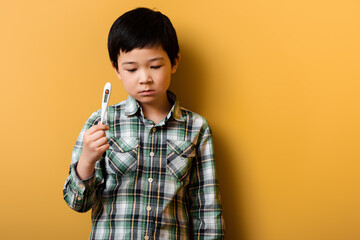sad asian boy holding thermometer on yellow