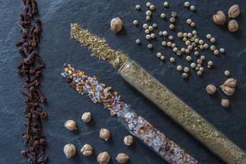 Various spices and herbs on a textured background. Set of spices and herbs. Pepper, salt, cloves, basil, cardamom. View from above. Spices in a glass flask