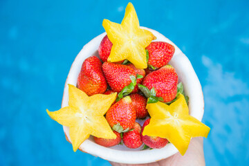 Strawberries and carambola are laid out in a half of coconut, on a blue background. Colorful,...