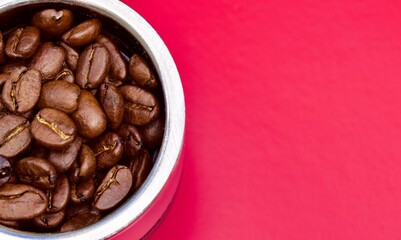 Close up image of coffee beans against a bright pink background.