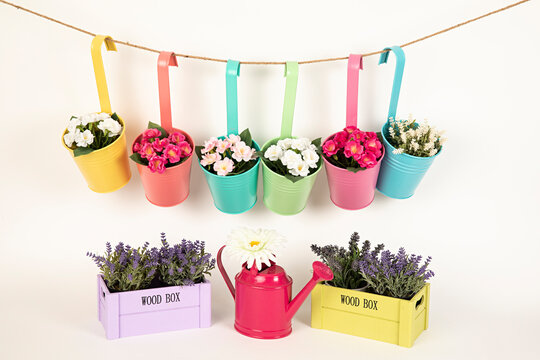 Maceteros de colores con flores y regadera rosa.