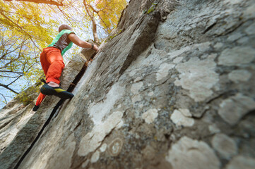 A man is training in free climbing on a rock stone in the forest on a sunny day. The concept of leisure activities of an active lifestyle of people aged