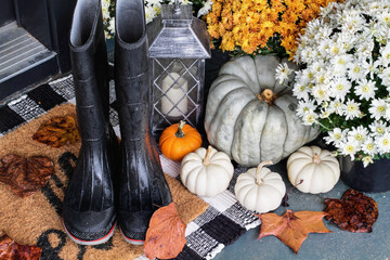 Rain boots on the front porch decorated for autumn with heirloom gourds,  white pumpkins, mums and...