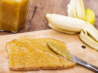 Banana jam on slice of bread with jar and piece of fruit, high angle view