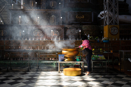 Offering to Buddha: barefoot woman burning incense. Rays of light entering the temple. Shwe Tha Lyaung Buddha reclining image, Bago, Myanmar, Burma, Southeast Asia