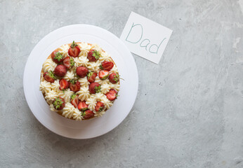 Cake with white cream and fresh strawberries on a gray background. Card - an inscription for dad. Father's day or birthday. Image with copy space, top view, horizontal orientation.