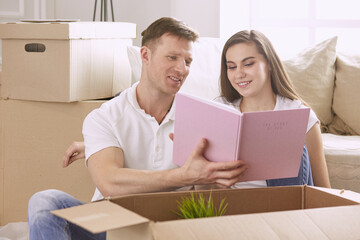 Portrait of happy couple looking at laptop computer together sitting in new house, surrounded with boxes