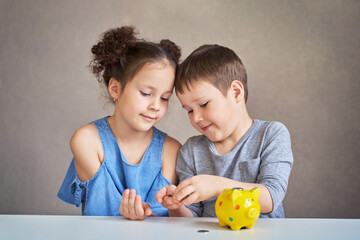 Fototapeta premium two children count money and put it in a piggy Bank