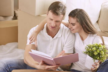 Portrait of happy couple looking at laptop computer together sitting in new house, surrounded with boxes