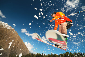 man skier in flight after jumping from a kicker in the spring against the backdrop of mountains and...