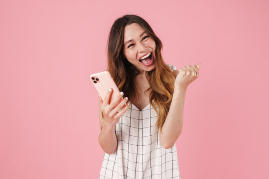 Image of excited cute woman using cellphone and making winner gesture