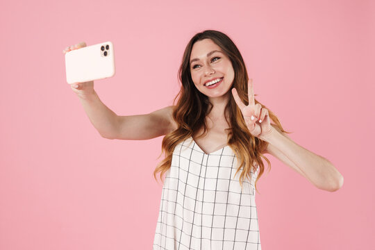 Image of woman gesturing peace sign while taking selfie on cellphone