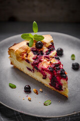 A piece of blackcurrant pie on a grey plate decorated with mint leaves