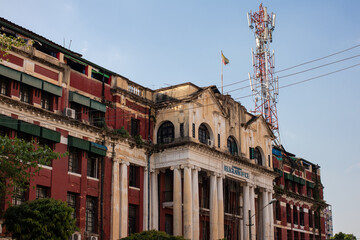 Fototapeta na wymiar Historical colonial building reconverted into an apartments house. Mobile communications antenna in the building. High columns at the entrance. Yangon - Rangoon, Myanmar - Burma, Southeast Asia