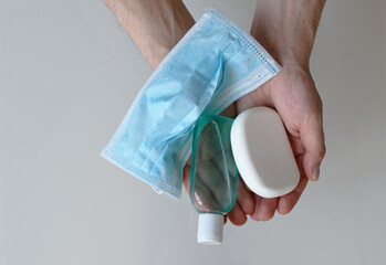 Man holding surgical mask, hand sanitizer and a soap, man's hands full of coronavirus prevention consumables isolated on white background
