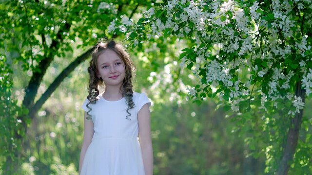 Smiling curly girl portrait in sunny garden on blooming fruit trees background. Happy girl model posing in blooming spring orchard