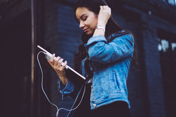 Charming stylish student with gorgeous brunette hair looking at textbook that holding in hands and walking in street.Young woman strolling with telephone.Promotional background for advertising message