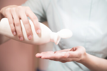 A professional beautician pours a white flacnaut cream mask on his hand to apply it to the client's face. The concept of using liquid masks in cosmetology